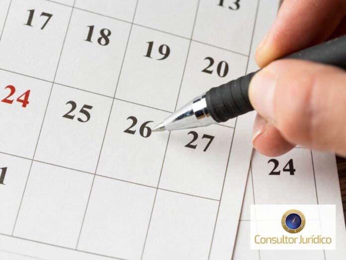 Mão com caneta marcando uma data em um calendário